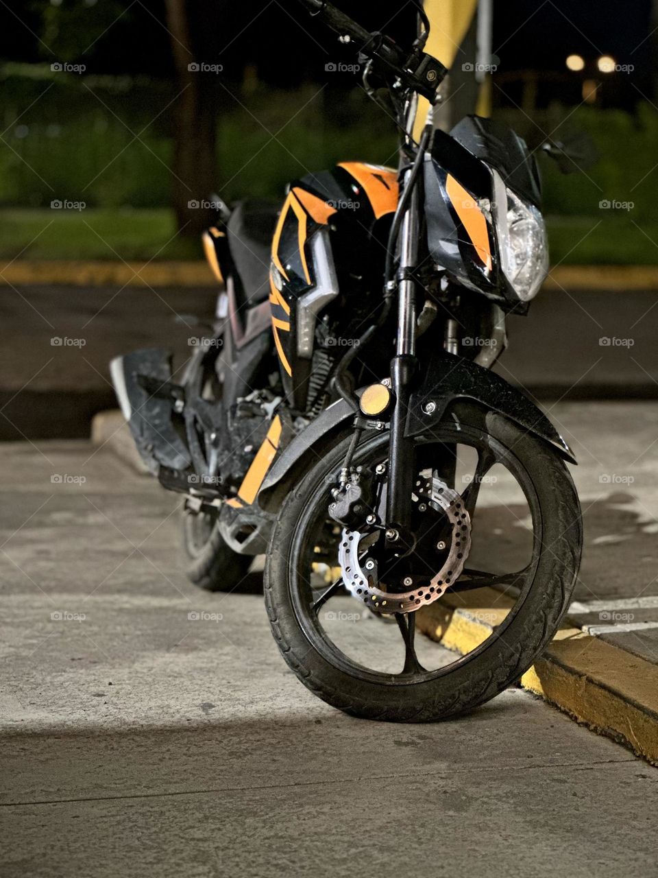 Black sport motorcycle with orange details closed-up, parked on the sidewalk at the midnight.