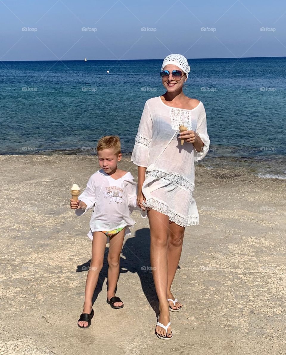 A young beautiful girl with a child walks on the sea in a polka-dot scarf