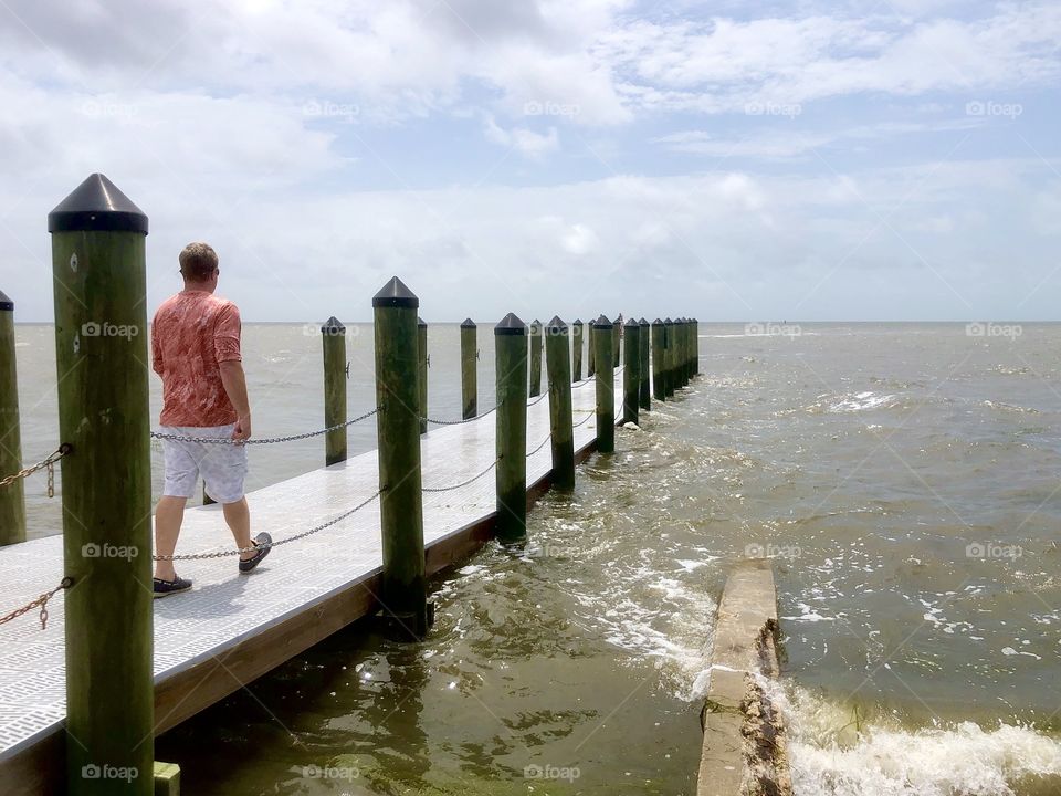 Man in shorts walking out fishing boat dock on sunny day in Gulf of Mexico 