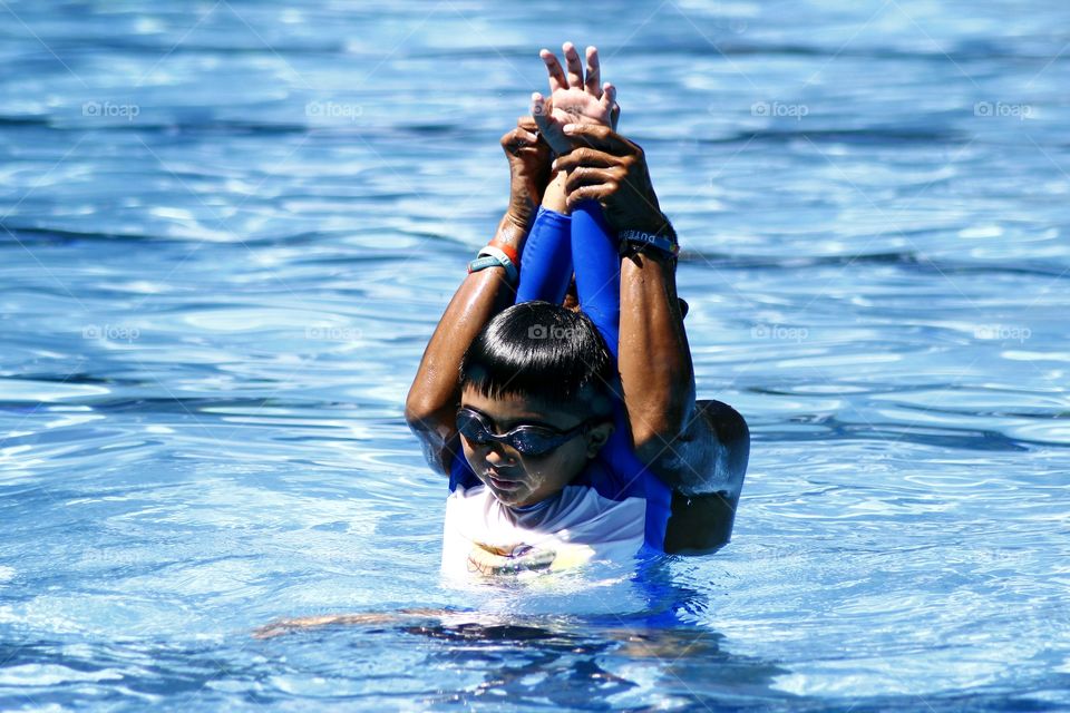 young kid learns how to swim with the help of a swimming coach