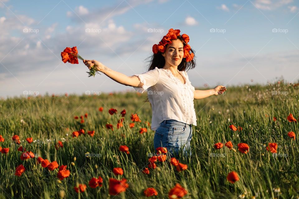 Beautiful woman, being happy while wandering around in a field of poppy flowers, at sunset time.