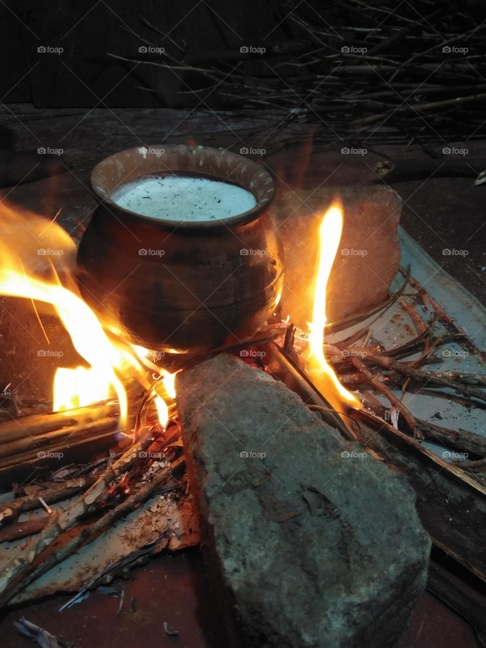 This is a capture of a boiling milk on a hearth.There is a clay pot with milk on the hearth and the hearth is made by three stones.There is burning woods with burning flames.Normally this type hearths can be seen at poor house in southern Asia.