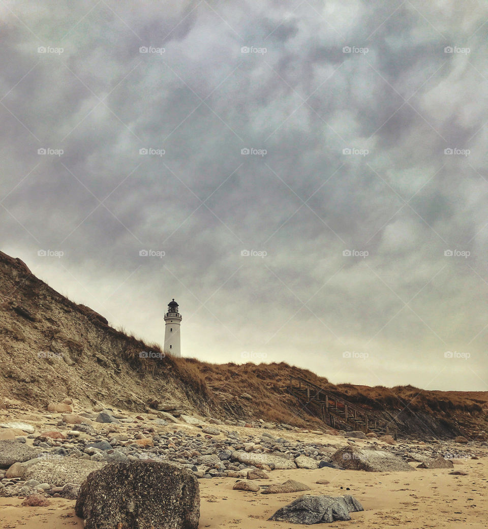 A lighthouse standing tall at the coastline on a cloudy afternoon