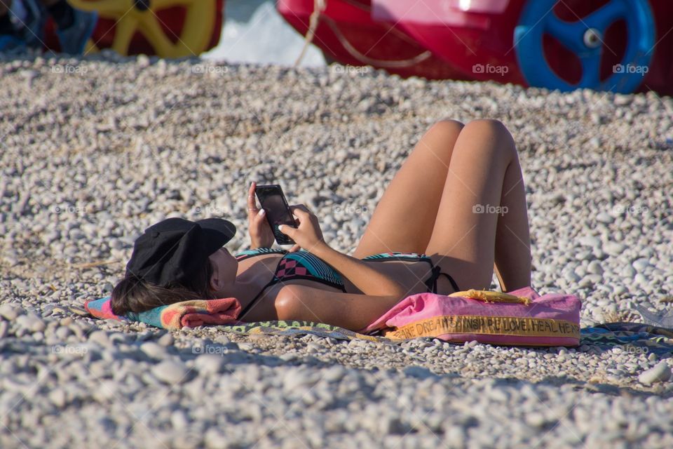 A woman relaxing on the beach in Spain, checking her phone while enjoying the sun 