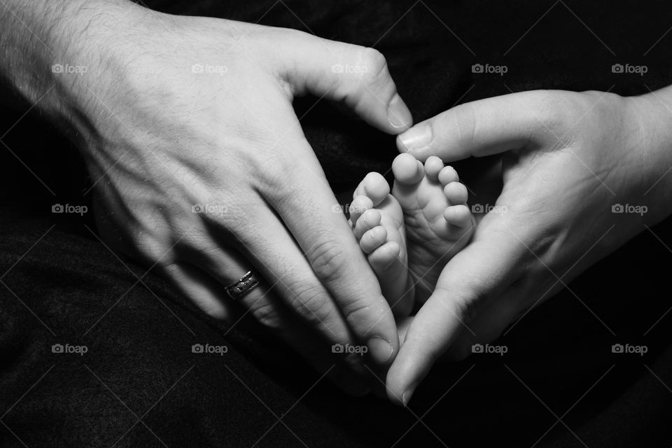 Father and mother’s hands making a heart shape with their infant sons feet in the middle 