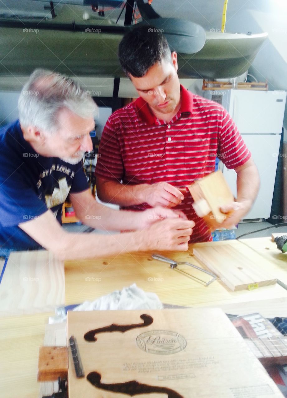 Father and son making a cigar box guitar in the garage.