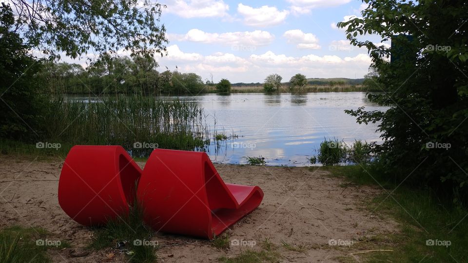 2 red recliners in front of a lake