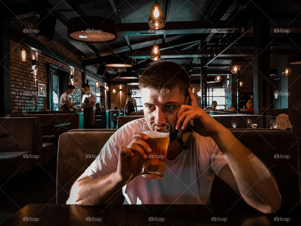 yong man drinking beer and talking with smartphone