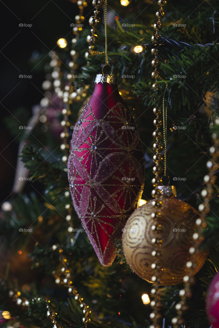A portrait of a christmas ornament hanging in a christmas tree surrounded by other decorations like chains, lights and christmas balls.
