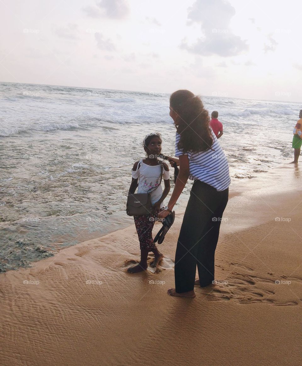 This is a capture of a sea beach.In this sunsetting time lot of people come to sea beach and these are two sisters in the sea beach. Elder one is tight on her younger 's hair. This is a scene reflecting the sister's love.๐