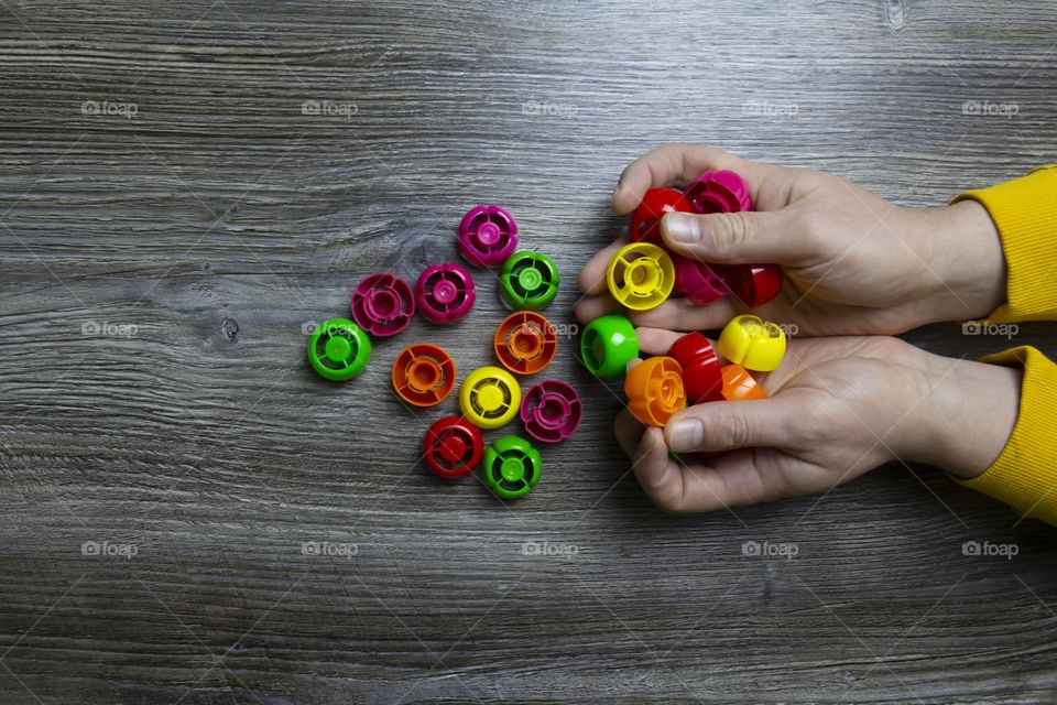 We collect garbage, plastic plugs and plastic to save our planet, nature and the environment. Men's hands lie on a gray wooden surface, which is used as a background or a surface with incident light.