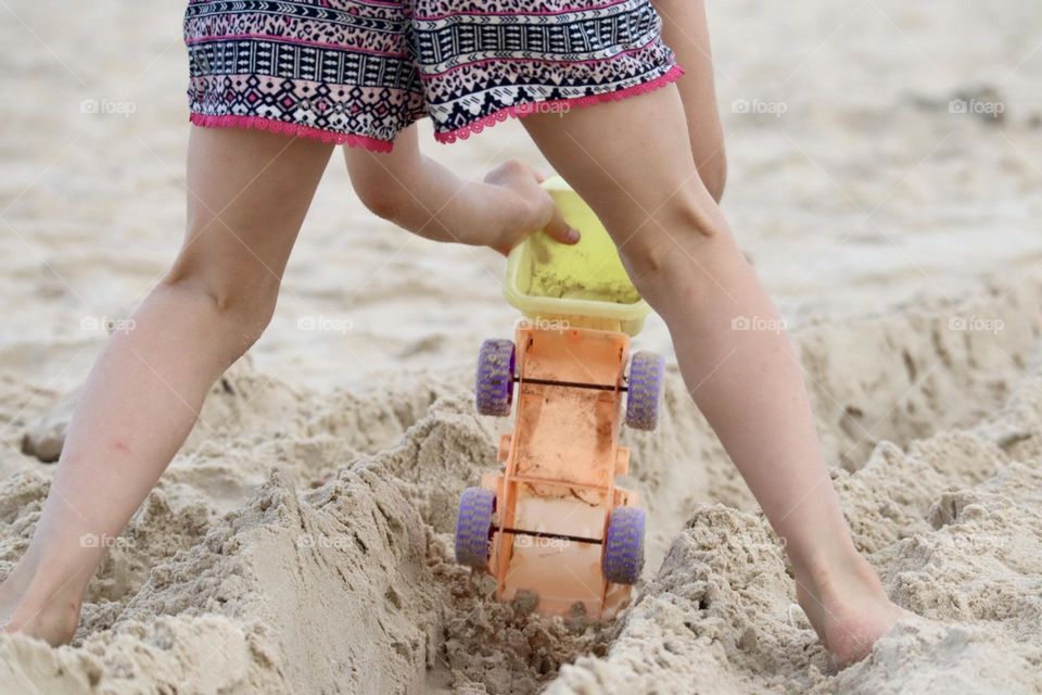 Girl playing with toy truck in the sand 