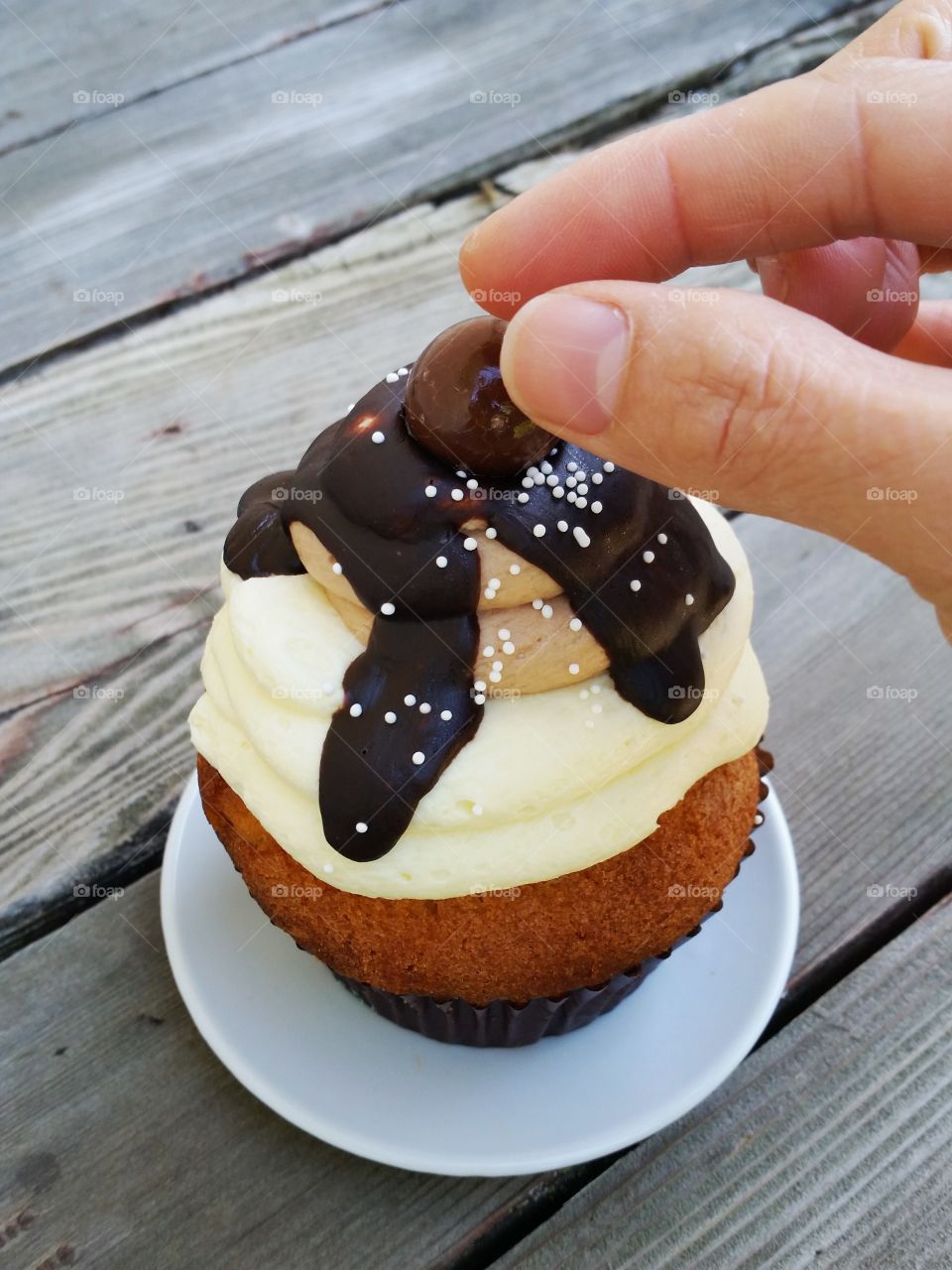 Salted caramel chocolate fudge cupcake, with hand applying garnish