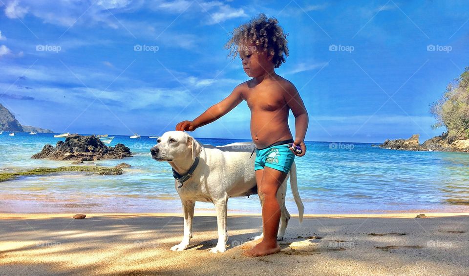 Boy touching dog standing on beach