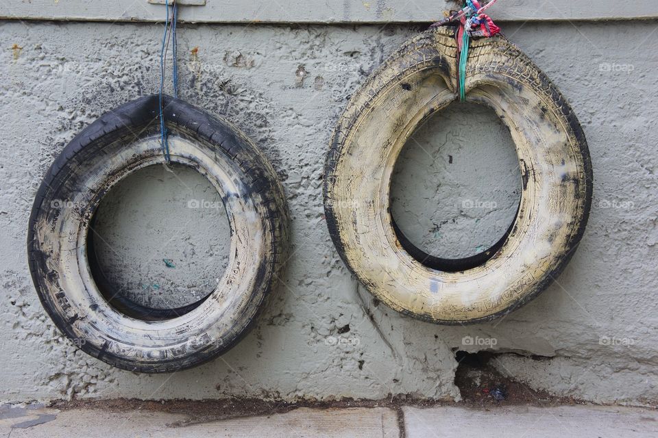 Two old worn tires hanging to cushion cars backing into the wall of the parking area in Brooklyn, NYC.
