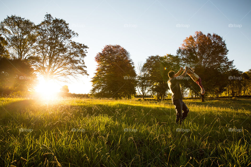 My favourite moment when a dad plays with his little girl. Image of dad swinging girl through the air at sunset in a meadow.