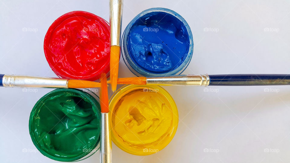 four colors of gouache in open containers, blue, green, red, yellow and four tassels on containers, top view