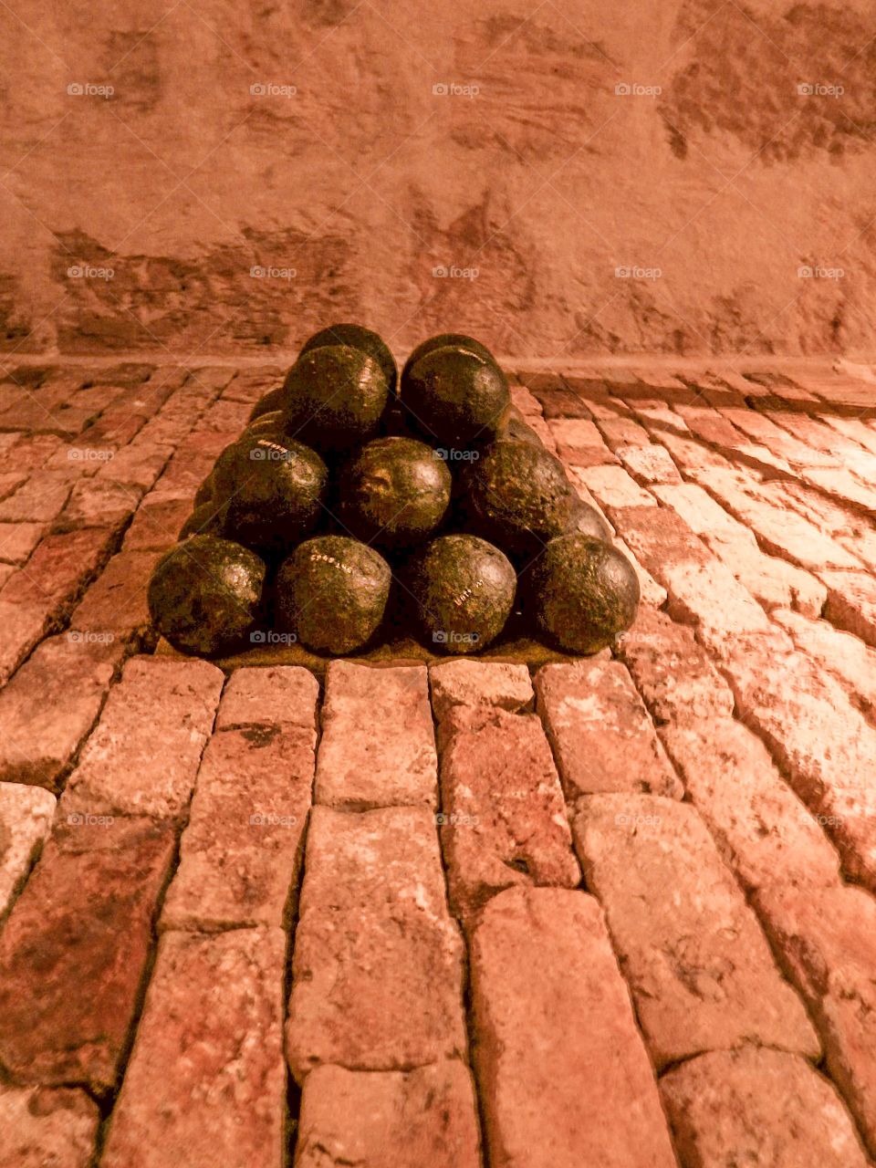 Still life of black cannon balls piled up nearly on a brick layered floor 