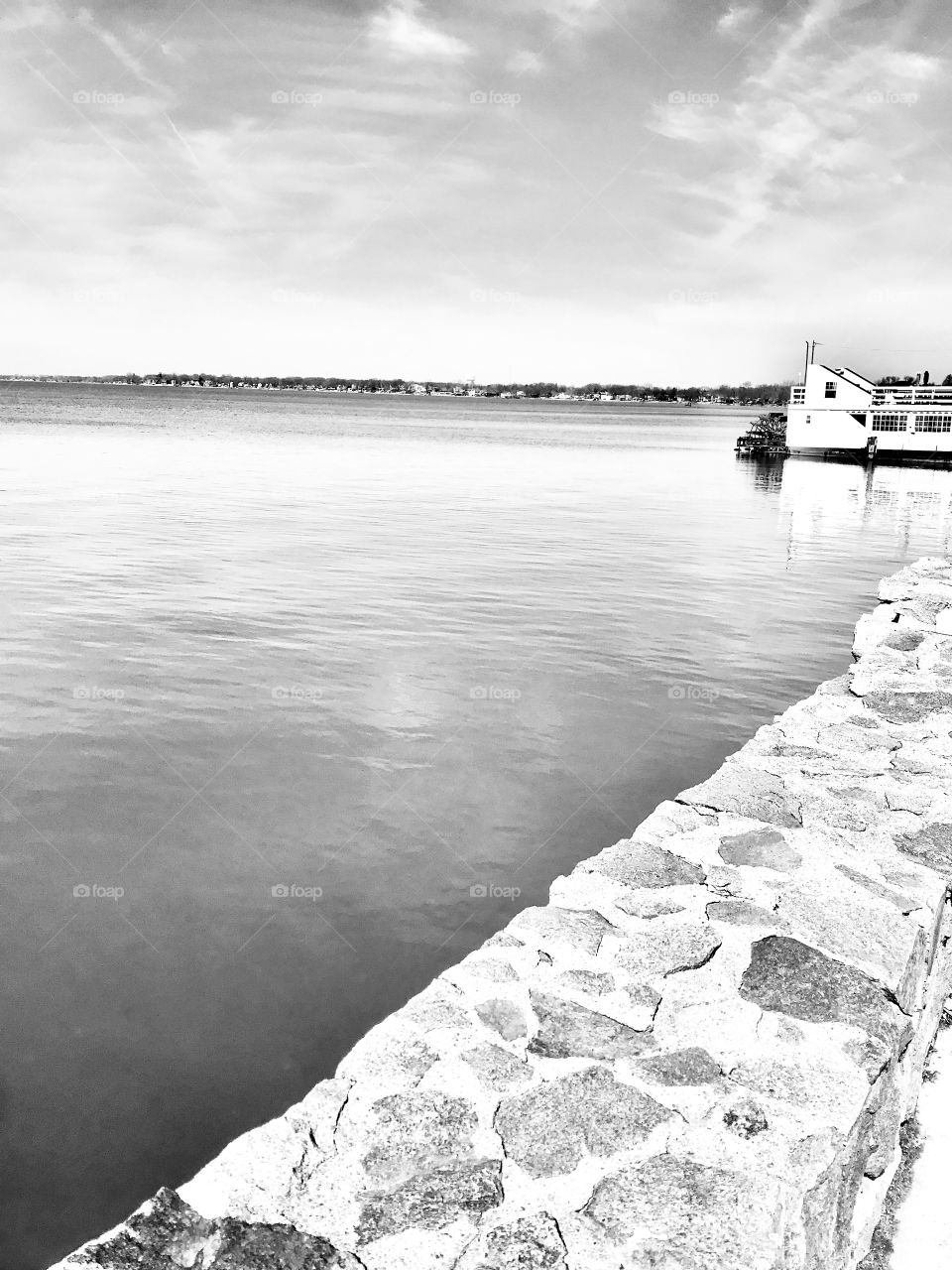 Serene black and white photo of seawall with smooth lake in background with ferry boat off to the side. 