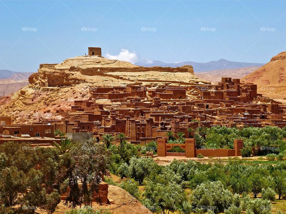 "A traditional Moroccan village built of red clay, surrounded by greenery and desert landscapes, showcasing cultural heritage."
