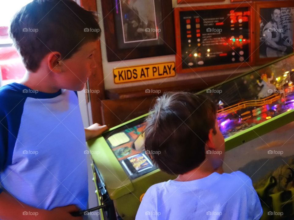 Boys Playing Pinball. Young Brothers Playing Pinball In An Arcade
