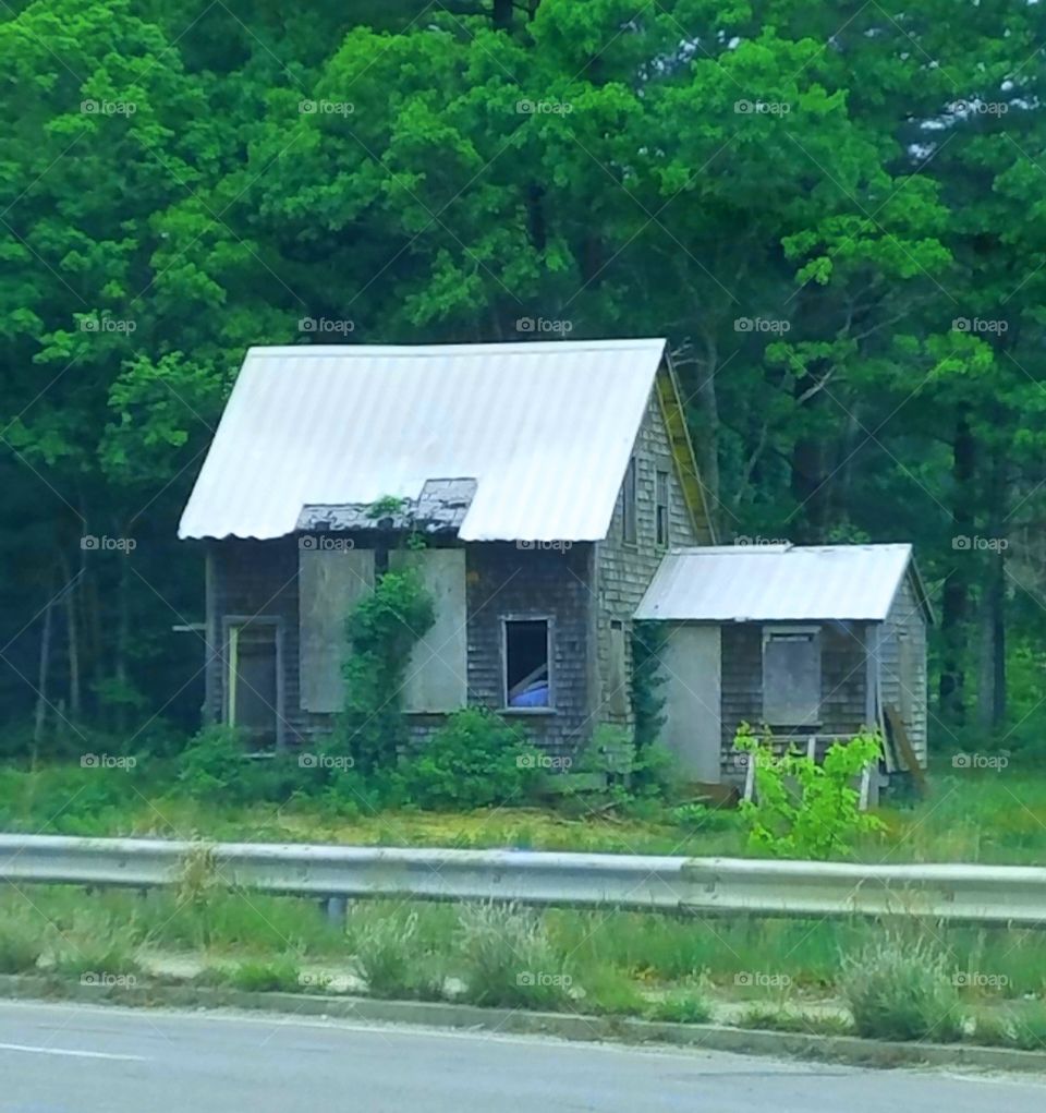 House abandoned & falling apart, seen off side of road.