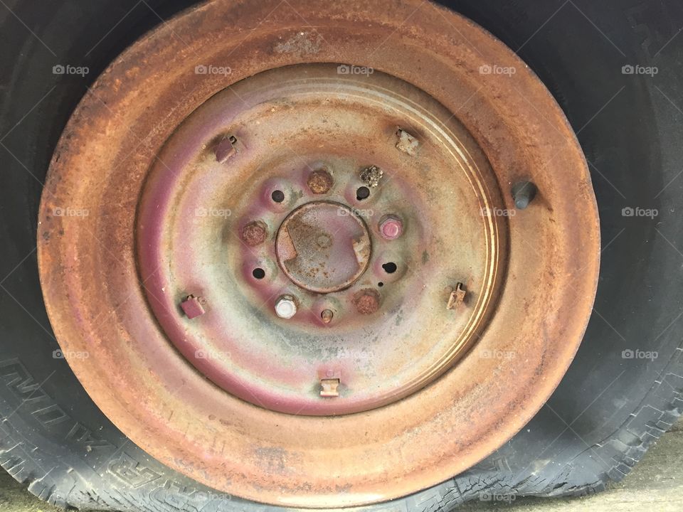 Flat tire and rusted metal wheel rim and lug bolts on a vintage vehicle