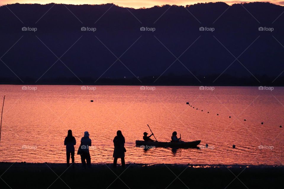 Silhouette of a kayak with people on board at a lake at sunset
