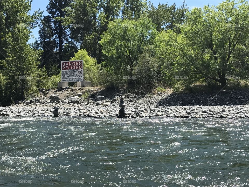 White water rapids on Wenatchee River. Zen stones stacked pretty high off the shore next to a Caution sign. 