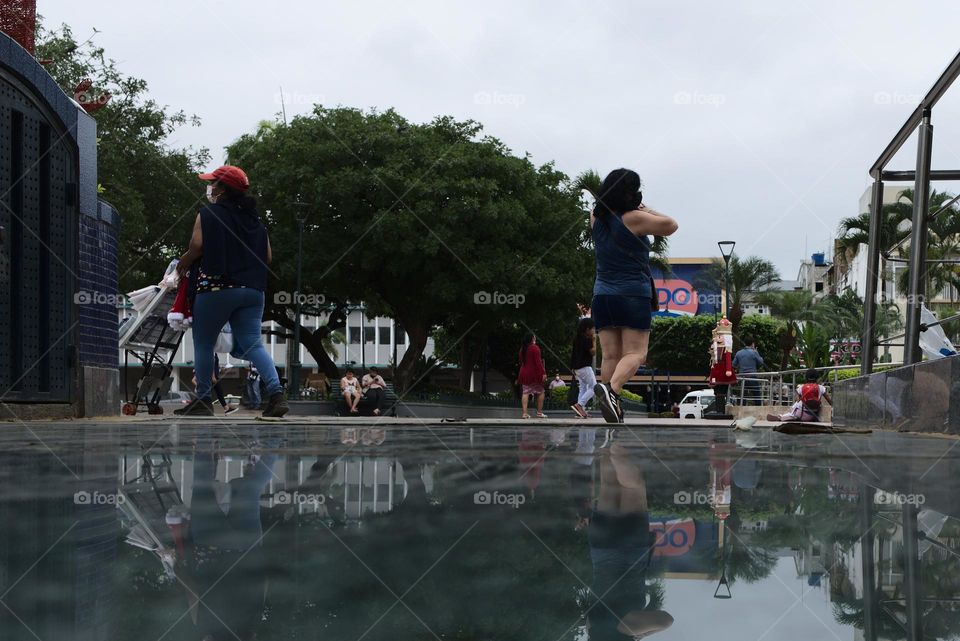 Reflected view of a park with people walking and enjoying a sunny day in the city.