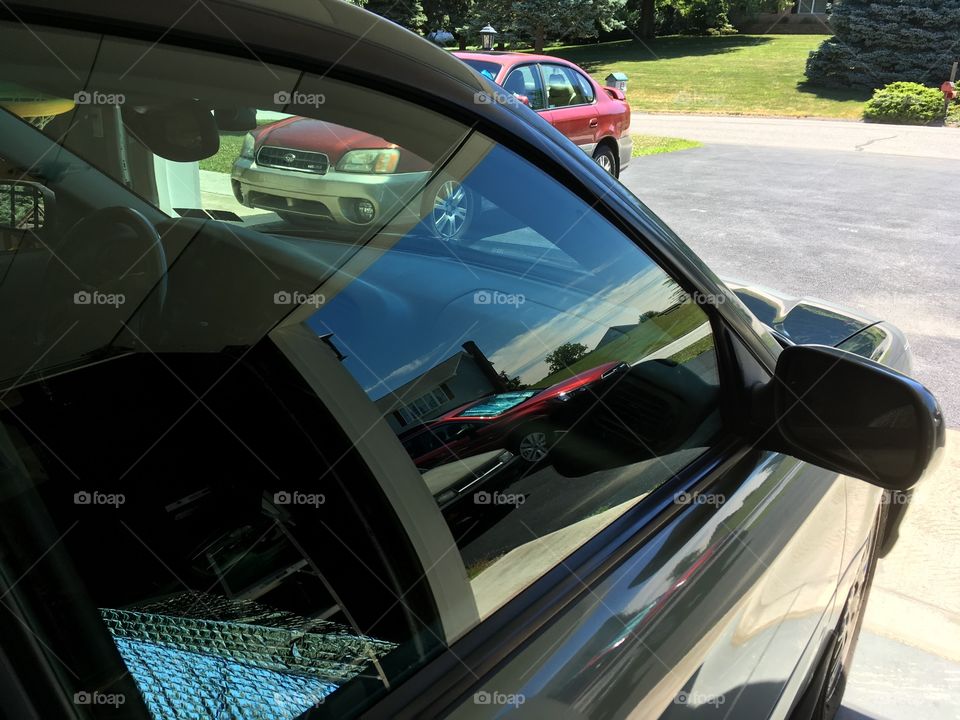 Two Subaru cars reflecting  in the window of a Subaru with another Subaru in frame. 