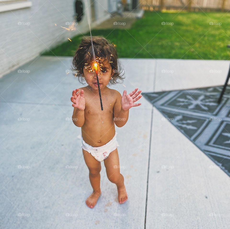 Baby clapping for fireworks on 4th of July, celebrating America, fireworks and sparklers in America, baby in the backyard, infant excited about fireworks, foreground focus on sparklers 