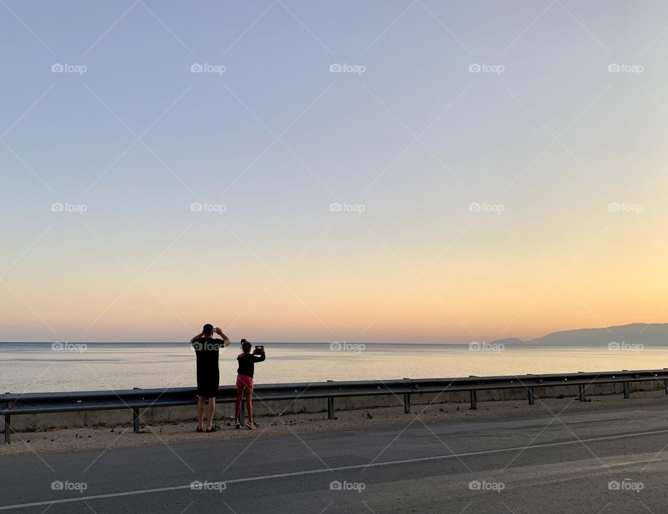 Dad and daughter taking pictures of the sunset