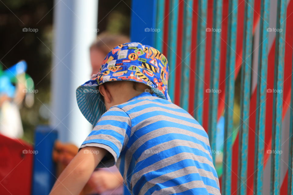 Little five year old boy wearing sunhat and striped tee shirt playing in playground in summer