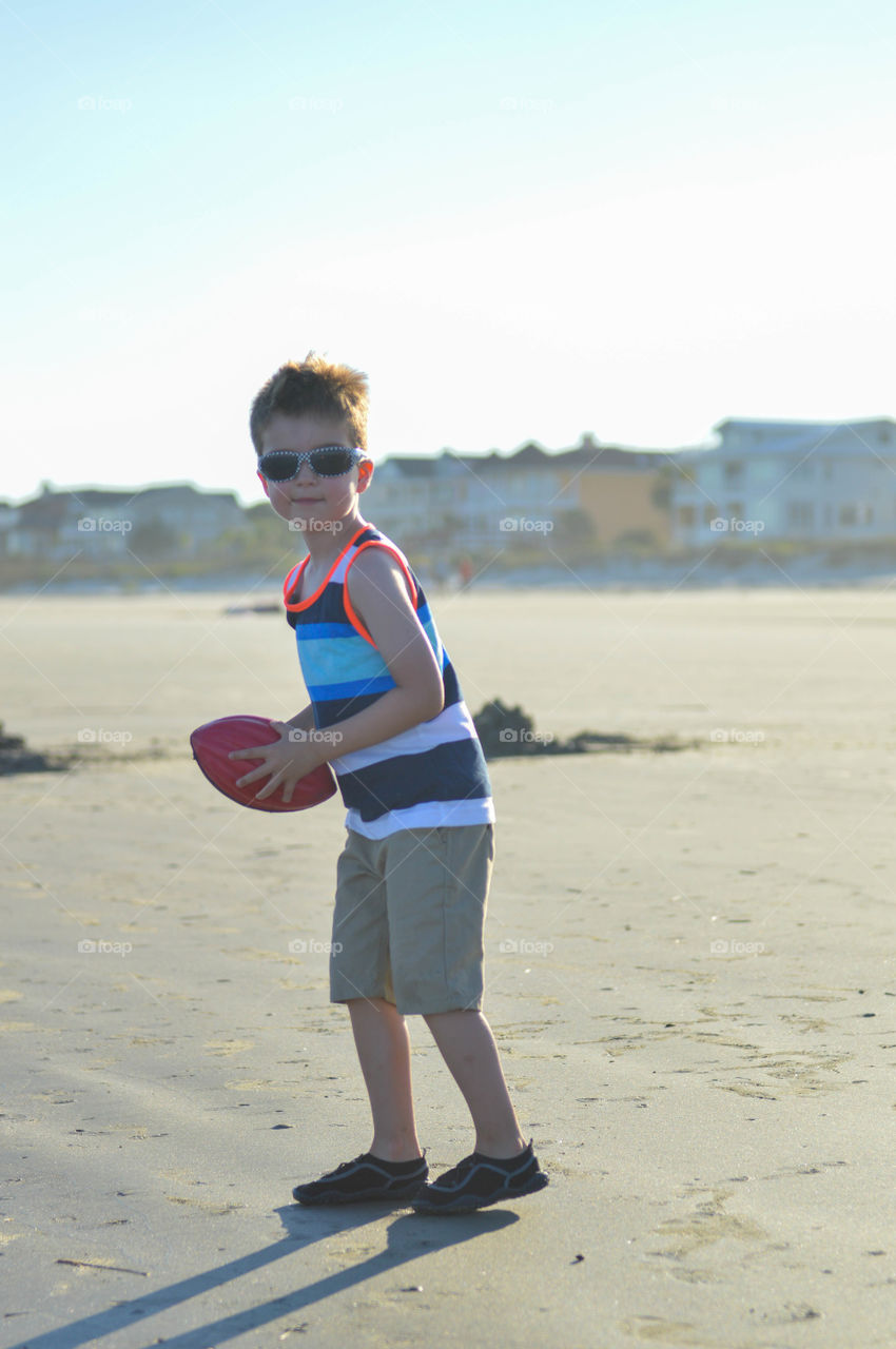 Young boy playing catch with a football on the beach at sunset