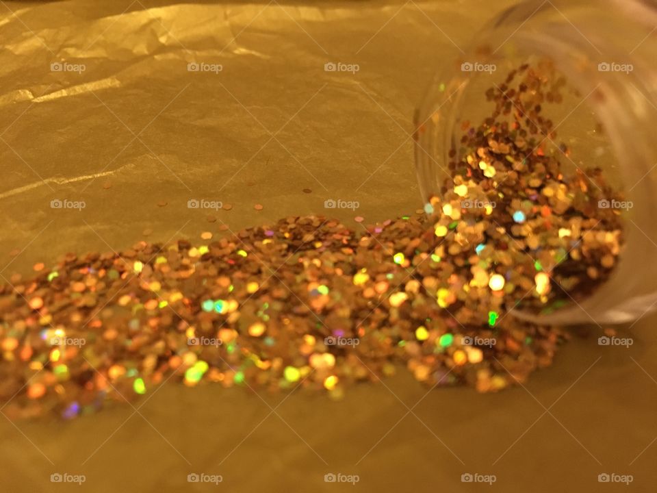 Close up view of gold glitter pieces spilled onto gold tissue paper 