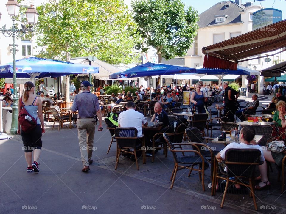 Crowds of people out walking, shopping, and eating, on Luxembourg streets on a summer day. 