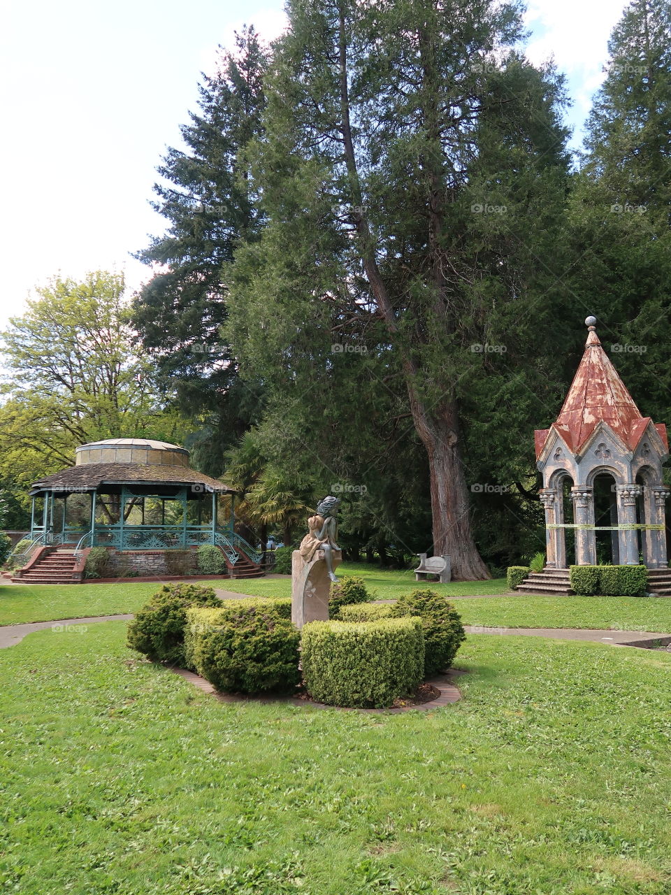 A nice little landscaped park with and old stone gazebo and a modern gazebo and a beautiful stone statue. 