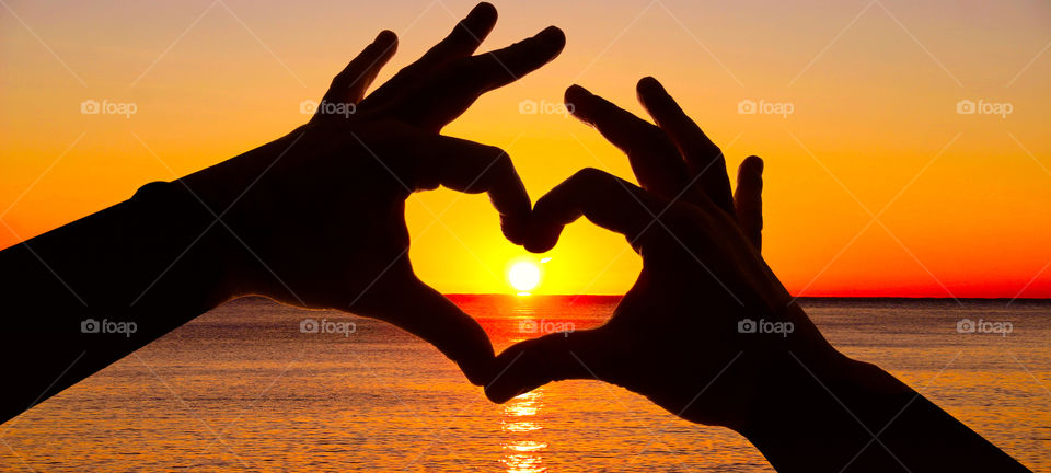 Silhouette hand in heart shape and sunrise on the ocean. Silhouette hand in heart shape and sunrise on the ocean