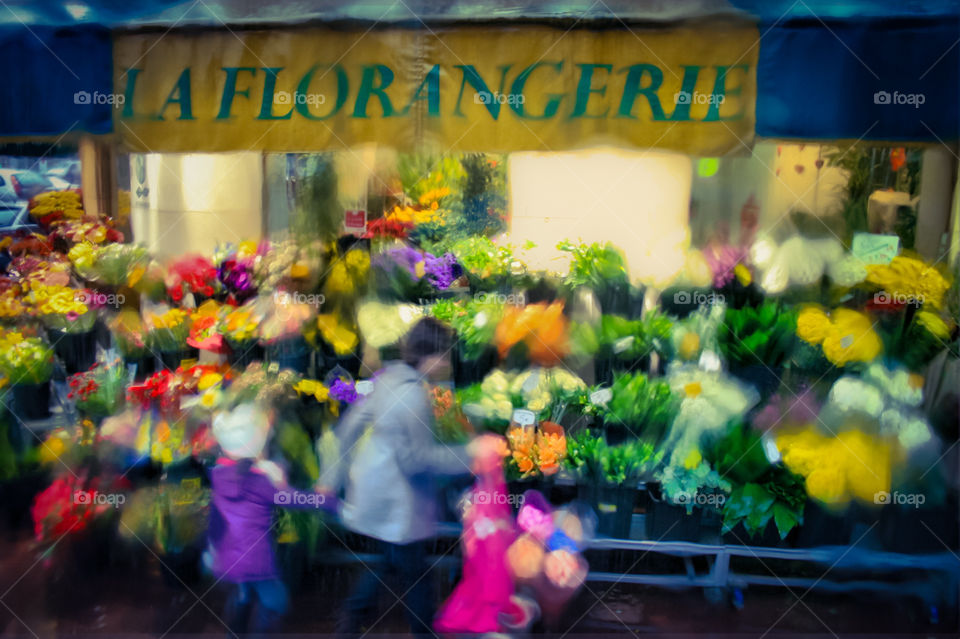 Rain pouring down a bus window, creates blurred colours in this view of a mother and child walking past a colourful florist on a wet day in Paris