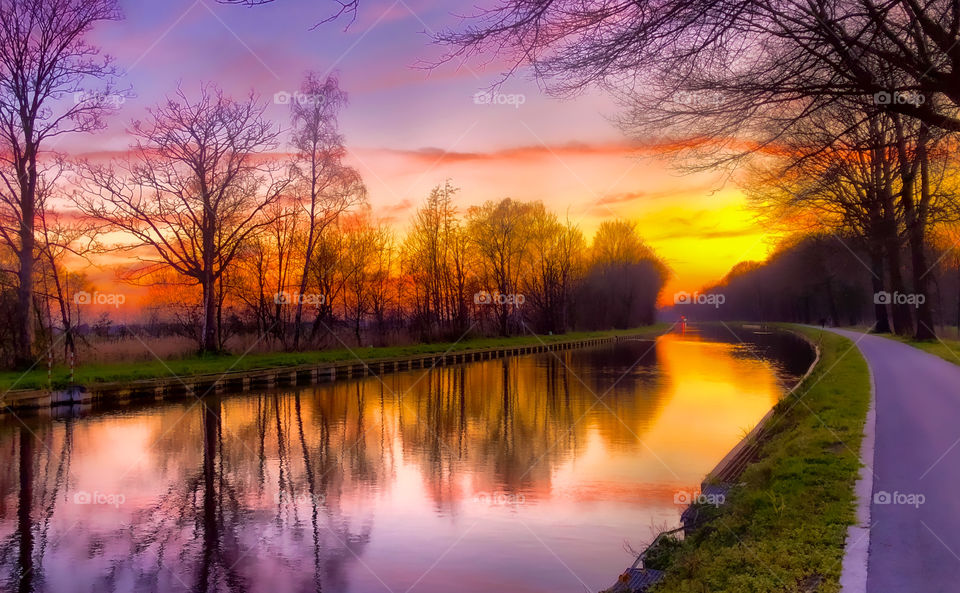 Dramatic and colorful sunset reflected on the water of the canal through the woods