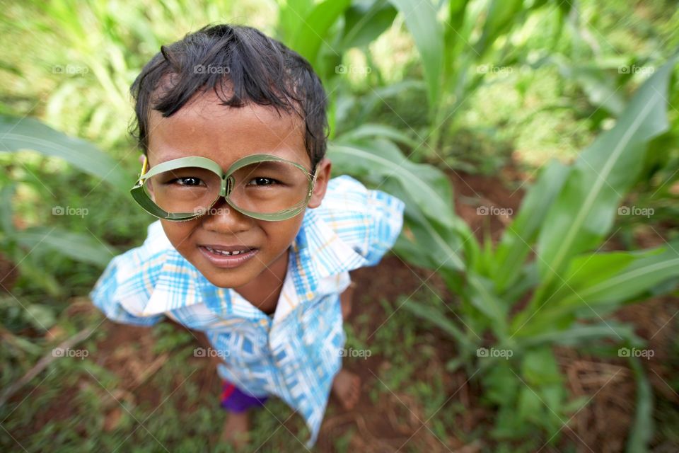 A small kid make a glasses. A small kid use the coconut leaf to make a glasses to wear for fun.