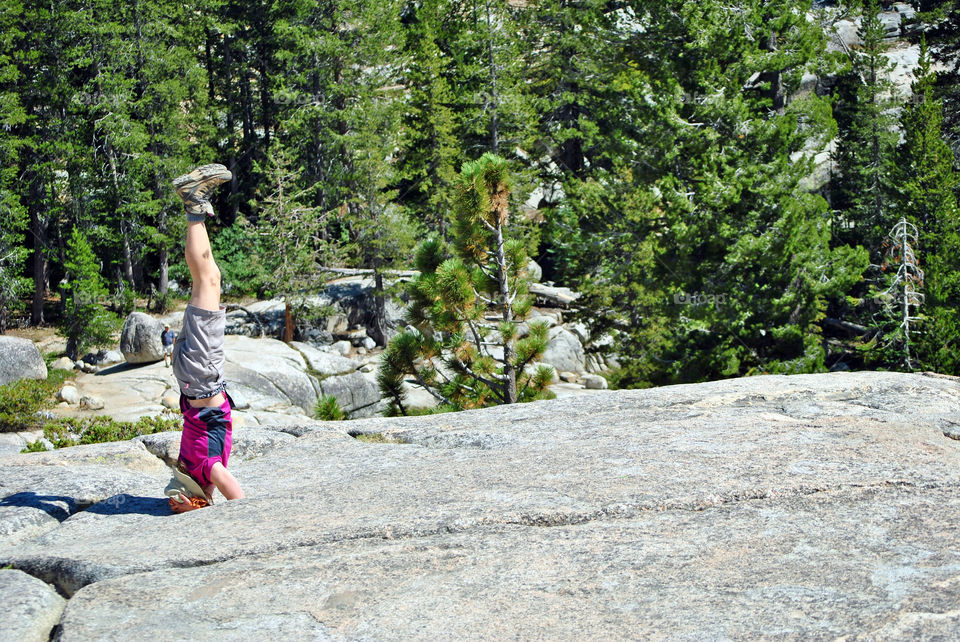 Girl doing a headstand on top of a rocky mountain, wearing hiking shoes