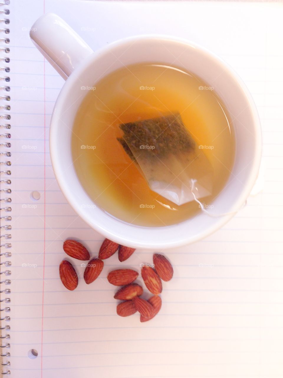 Tea and snack. A cup of tea brewing on a spiral notebook. A handful of almonds sits next to the mug of tea, waiting for an afternoon work break.
