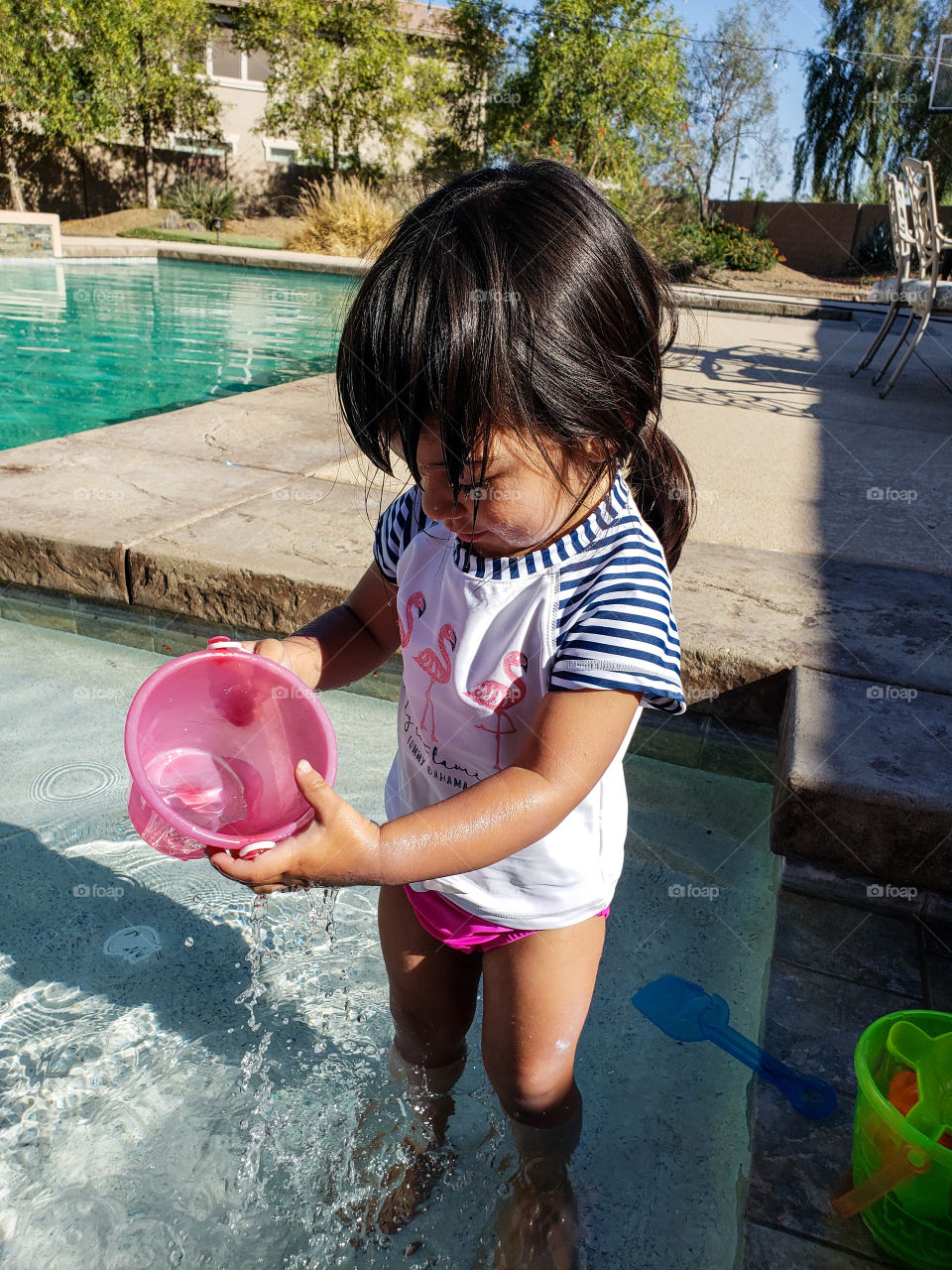 Toddler wearing swimsuit playing with bucket in the pool