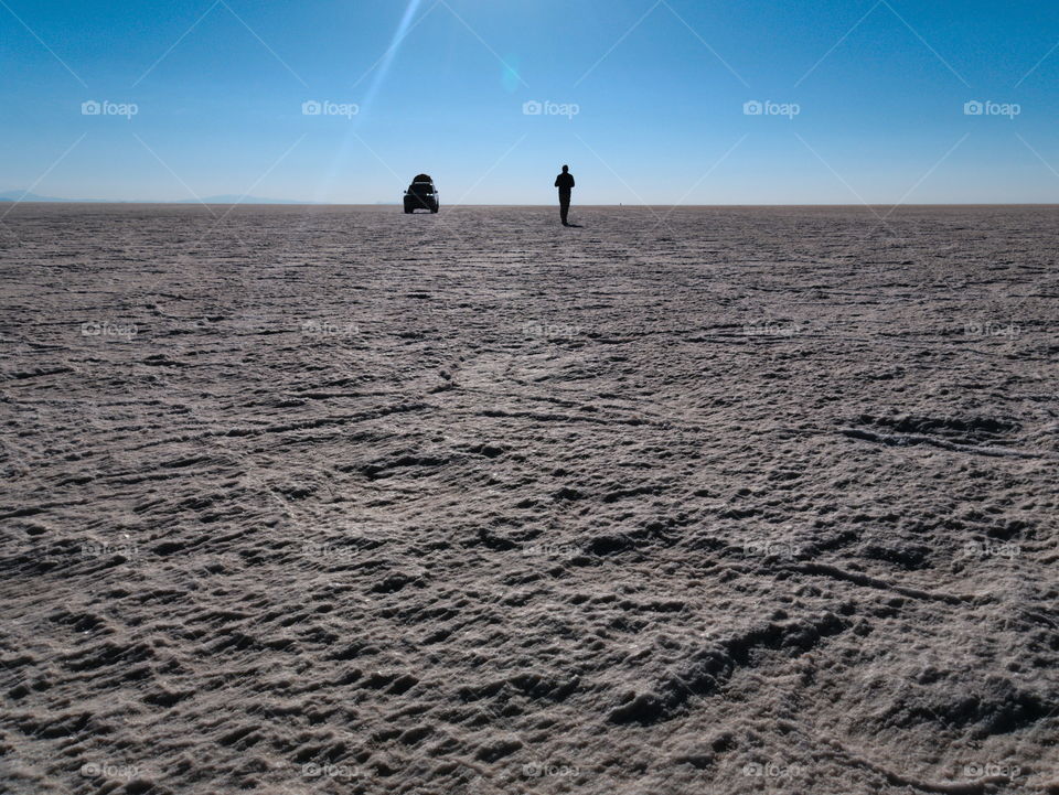 Lonely man and his car in the middle of a huge salt flat