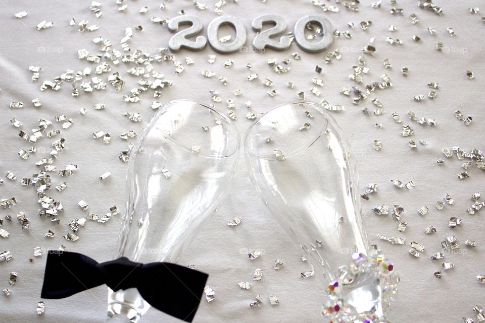 Conceptual overhead view of champagne glasses representing a man and a woman with the year ‘2020’ in silver with silver confetti on a white background - landscape format