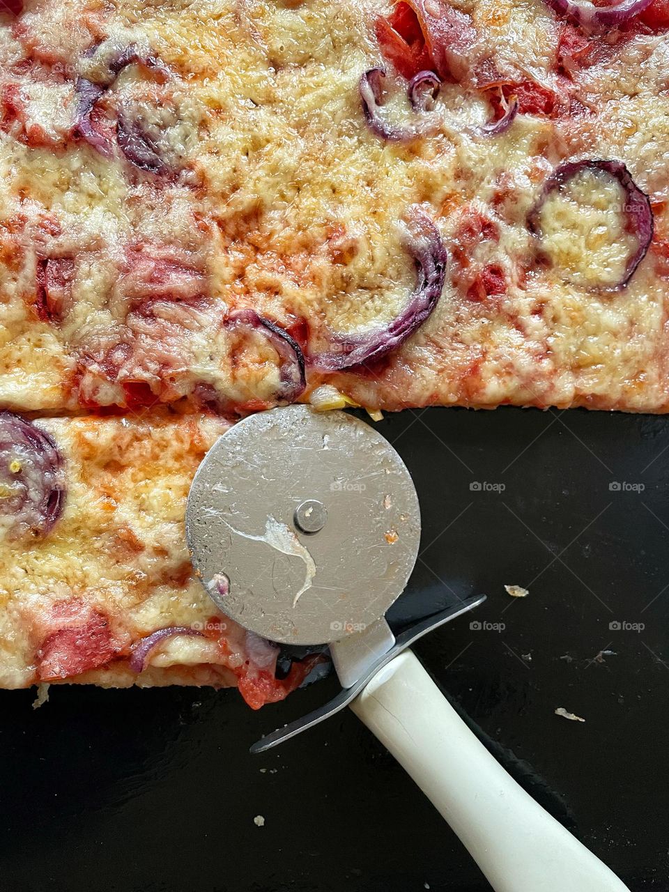 Close-up of a homemade salami pizza on baking sheet with pizza cutter