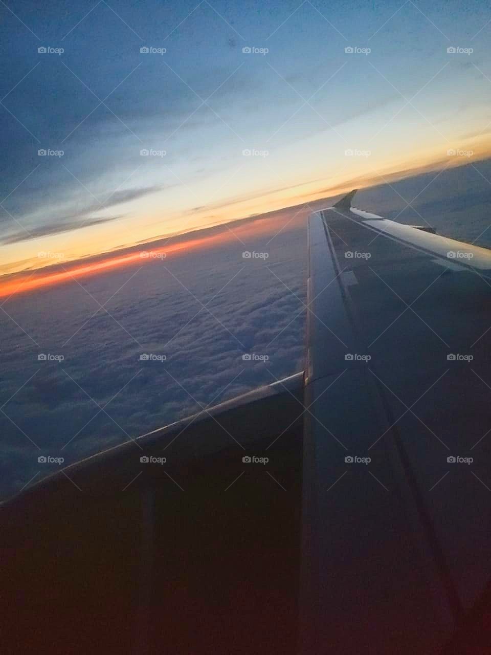 The plane is gaining altitude.  A carpet of clouds over the plane.  Sunset