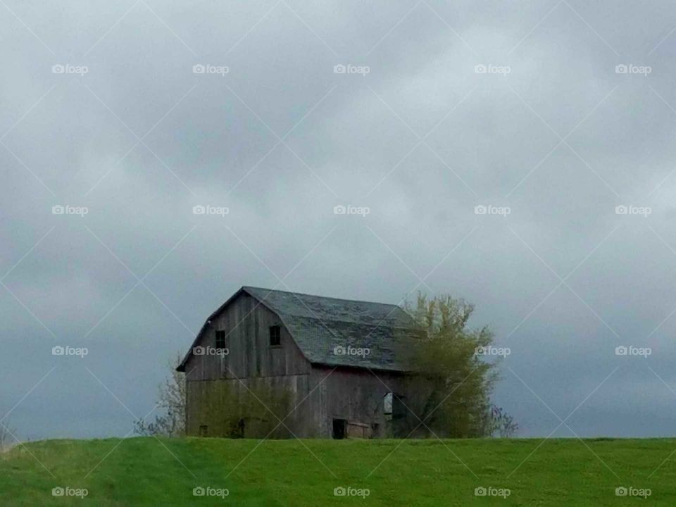 Abandoned barn on grass against cloudy sky